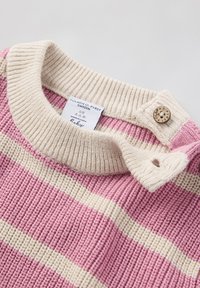 Neulepaita, jossa on vaaleanpunaisia ja kermaisia raitoja, ribbikuvio, kermavärinen kaulus ja nappisuljenta. Tunnuksessa lukee "POLARN O. PYRET."