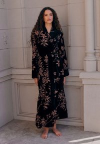 Juodos aksominės suknelės su ilgomis rankovėmis, puošta sudėtinga gėlių siuvinėjimo raštu rožinės spalvos atspalviais. Suveržta liemens juostele, atitinkančia spalvą.