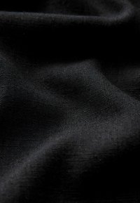 Musta kangas sileällä pinnalla, jossa on hienovarainen kudos. Materiaali näyttää kevyeltä, pehmeillä laskoksilla ja luonnollisella roikkuvalla ilmeellä.