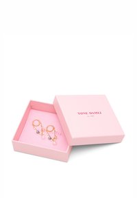 Pendientes en tono dorado con cuentas de colores y detalles colgantes exhibidos en una caja de color rosa claro, con el nombre de la marca en relieve en dorado.