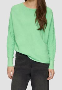Mintgrüner gerippter Pullover mit überschnittenen Schultern und langen Ärmeln, kombiniert mit schwarzen Jeans. Weicher Stoff mit einem entspannten Schnitt.