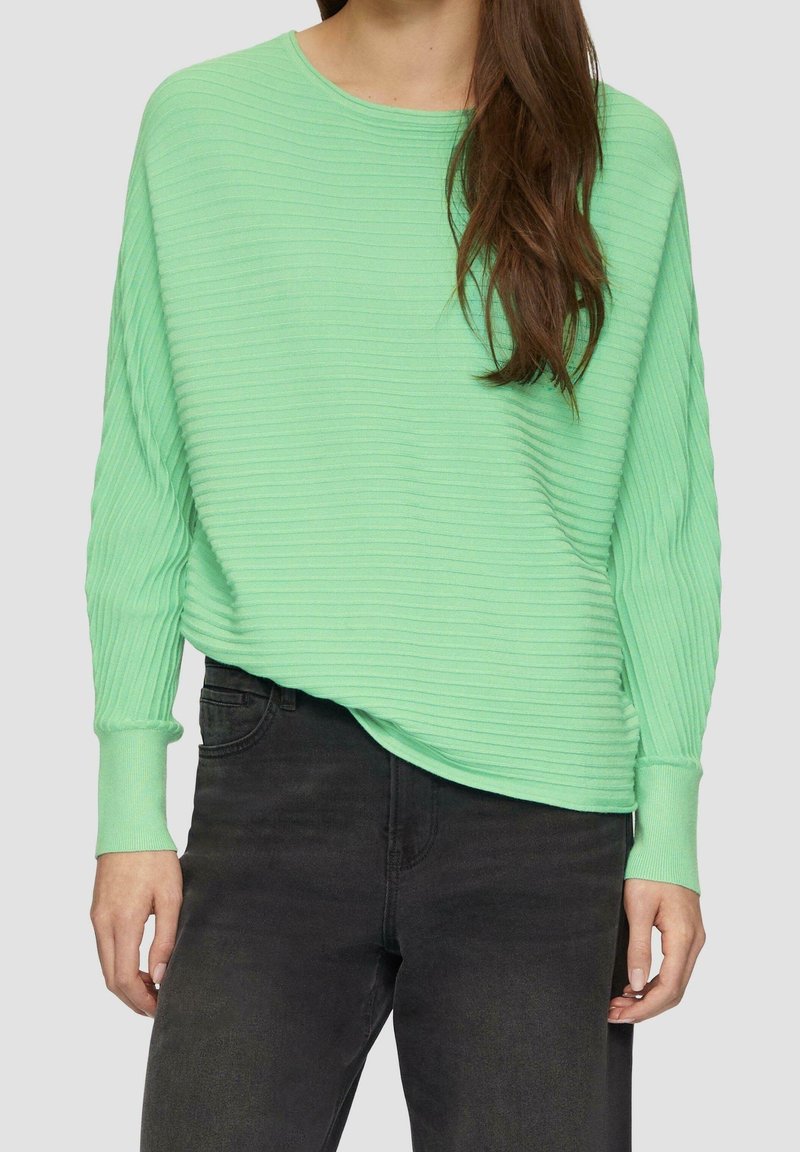 Mintgrüner gerippter Pullover mit überschnittenen Schultern und langen Ärmeln, kombiniert mit schwarzen Jeans. Weicher Stoff mit einem entspannten Schnitt.