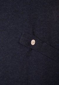 Tissu tricoté bleu marine avec un motif texturé et un détail de bouton clair sur le côté gauche.
