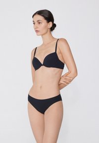 Černý bikiny set obsahuje podprsenku s tvarovanými košíčky, nastavitelné ramínka a hladké, nízké kalhotky. Materiál se zdá být hladký s jemným protažením.
