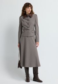 Brown houndstooth suit with a fitted jacket, brown collar, belted waist, and a flowing skirt, paired with knee-high brown boots.