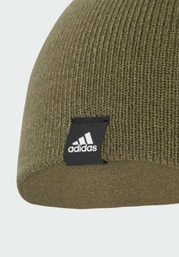 Olive green knitted beanie hat with ribbed texture and a black rectangular tag featuring the Adidas logo on the side.
