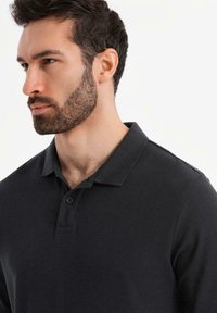 Mörkgrå polo t-shirt i texturerad tyg, med klassisk krage, treknappsstängning och korta ärmar. Inga synliga mönster.