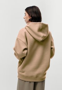 Felpa oversize beige realizzata in tessuto morbido, con un grande cappuccio, spalle scese e polsini e fondo a coste.