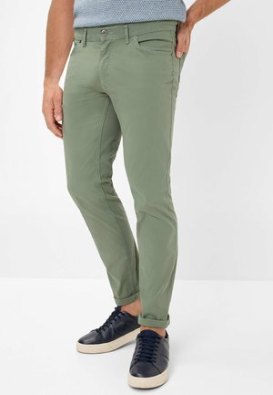 Light green cotton trousers with a slim fit, featuring a button closure, front pockets, and rolled cuffs. Paired with dark blue sneakers.