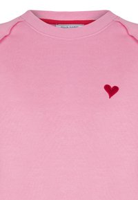 Rosa sweatshirt med rund halsringning och raglanärmar. Har ett litet röd broderat hjärta på bröstet, tillverkat av mjukt material.