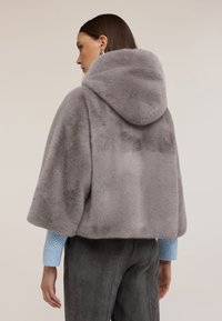 Szara peleryna z kapturem z sztucznego futra z krótkimi rękawami; miękka tekstura, gładka powierzchnia, w połączeniu z jasnoniebieskim, teksturowanym swetrem i ciemnymi spodniami z korduroy.