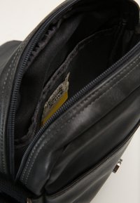 Interno di una borsa in pelle nera con chiusura a zip, caratterizzato da una texture morbida e un'etichetta visibile in giallo e grigio.