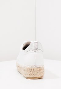 Vit sneakers med en metallisk silveraccent på hälen, vävd jute-mellansula och slät läderöverkonstruktion. Rundad form, minimalistisk design.