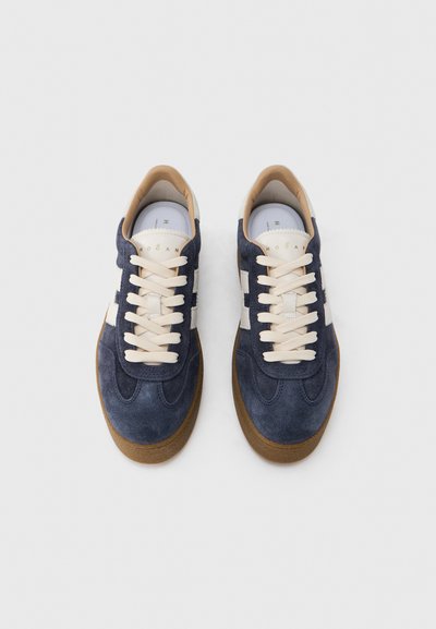 Ναυτικά σουέντ αθλητικά παπούτσια με κρεμ κορδόνια και λευκές πλευρικές ρίγες. Λαστιχένια σόλα, στρογγυλή μύτη και χρυσό λογότυπο στη γλώσσα. Υφασμάτινο επάνω μέρος με υφή.