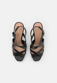 Sandales à talons noires avec tige synthétique texturée, bout carré et plusieurs brides croisées. Bride de cheville réglable avec ferrures métalliques.