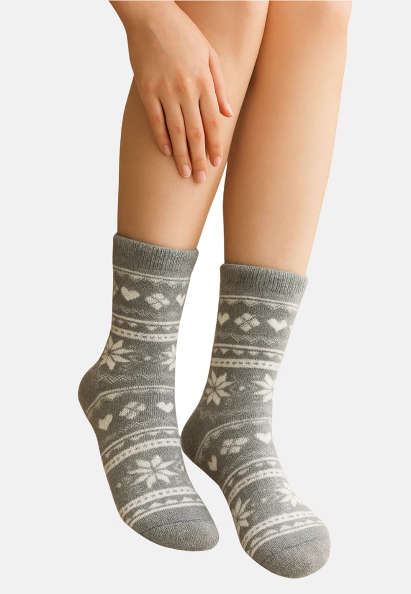 Legs wearing gray socks with white snowflake and heart patterns, one hand resting gently on the thigh against a plain background.