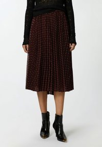 Jupe midi plissée bourgogne avec des pois bleu clair, en tissu léger. Assortie à des bottines noires avec des accents dorés.