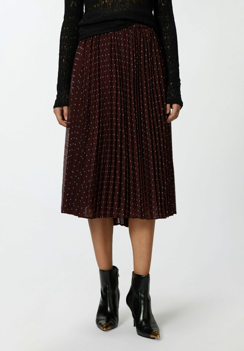 Jupe midi plissée bourgogne avec des pois bleu clair, en tissu léger. Assortie à des bottines noires avec des accents dorés.