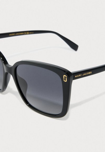 Svarte firkantede Marc Jacobs solbriller med mørke gradientlinser og gulllogo på tempel, på hvit bakgrunn.
