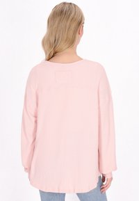 Top in maglia waffle rosa chiaro con maniche lunghe, orlo arrotondato e una piccola etichetta sul retro. Tessuto morbido, design casual, adatto per il layering.
