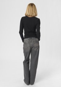 Crni rebrasti longsleeve top uparen s visokim strukom, širokim sivim trapericama. Glatka tekstura, jednostavan dizajn i bez vidljivih ukrasa.