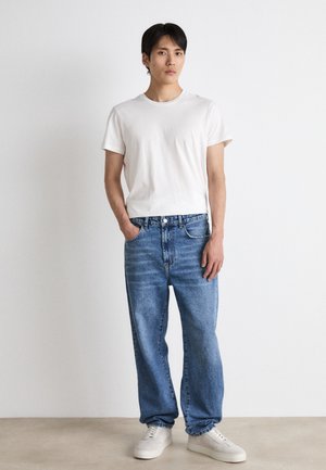 Hvit bomulls T-skjorte kombinert med lyseblå denimjeans. Slim-fit silhuett med en falmet vask, complementert med nøytrale sneakers.