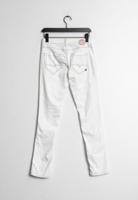 Jeans de mezclilla blanca colgando de una percha negra, con un corte ajustado, dos bolsillos traseros con detalles de costura y una etiqueta redonda de logo.