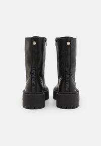 Bottines noires en cuir avec une semelle épaisse, fermeture éclair et un logo en relief sur le côté. Texture lisse avec une finition mate.
