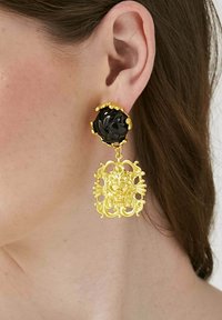 Boucles d'oreilles en ton doré présentant un clou en forme de rose noire avec un design doré orné suspendu en dessous. Les détails complexes rehaussent l'apparence générale.