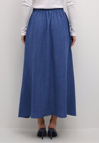 Blå maxikjole lavet af tekstureret stof, med elastisk talje og et flydende design, parret med mørkeblå højhælede sko.