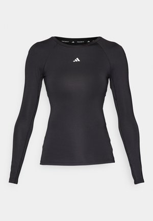 Cămașă sport neagră cu mâneci lungi, dintr-un material neted, cu un design mulat și cu un logo alb pe piept și în interiorul gulerului.