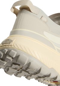 Gros plan de la semelle épaisse beige et crème ainsi que de la languette de talon sur une basket robuste avec un profil texturé pour l’adhérence.