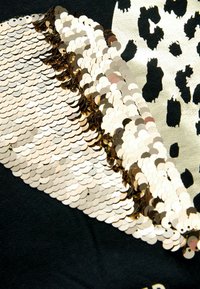 Țesătură neagră cu o aplicație de paiete aurii ce formează un model diagonal, alături de un detaliu cu imprimeu leopard într-o culoare contrastantă.
