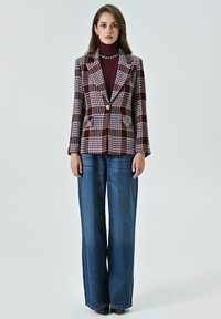 Blazer à carreaux dans les tons bordeaux, blanc et marine avec une fermeture à un bouton, associé à un jean en denim à jambes larges. Tissu lisse avec une coupe structurée.