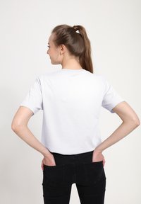 Weißes Baumwoll-T-Shirt mit kurzen Ärmeln, rundem Ausschnitt und lockerem Schnitt, kombiniert mit hochgeschnittenen schwarzen Jeans mit Gesäßtaschen.