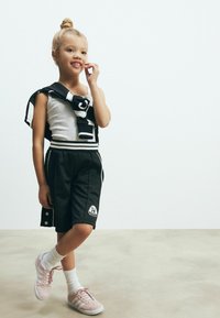 Sorte shorts med hvide striber, grå tanktop og et sort-hvidt omslag. Lyserøde træningssko med hvide striber. Glat, afslappet design.