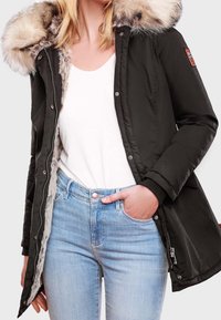 Sort parka-jakke med en faux fur hætte, lynlås foran og ribbede manchetter, parret med en hvid top og lyseblå jeans.