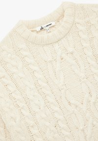 Cremefarvet kabelstrikket sweater med rund hals, tekstureret mønster og dekorerende kunstige perler jævnt fordelt over stoffet.