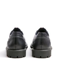 Scarpe in pelle nera con finitura liscia, suole in gomma e cuciture bianche a contrasto. Presentano un accento rosso e blu sulla linguetta del tallone.