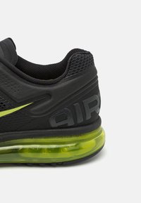 Shoe atlético preto com parte superior em malha, detalhes em verde-lima e uma unidade de amortecimento de ar visível. Apresenta um acabamento texturizado e detalhes de marca.