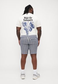 Hvid t-shirt med blå drueklase grafik og tekst, parret med flerfarvede stribede shorts i blå og hvid. Sportssko fuldender outfittet.