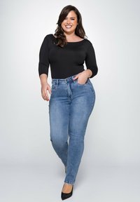 Schwarzer langärmeliger Body, kombiniert mit hochgeschnittenen blauen Jeans. Das Outfit zeichnet sich durch eine schlanke Passform, eine glatte Textur und ein klassisches Design aus.