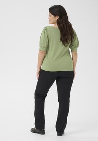 Green short-sleeve top with puffed sleeves, rounded neckline, and black trousers. Smooth texture and fitted design with subtle stretch.