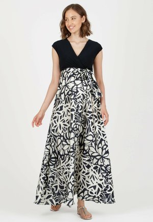 Maxikleid mit eng anliegendem schwarzen Oberteil und fließendem weißen Stoff, der große schwarze Blumenmuster aufweist. Mit gebundenem Taillen-Detail und Knöchellänge.