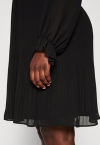 Robes plissées noires avec de longues manches volantes et un ourlet fluide. Texture transparente avec un éclat subtil, détails au niveau des poignets des manches.