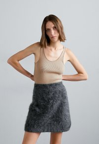 Un tricou fără mâneci bej, cu dungi, asociat cu o fustă mini gri închis, pufoasă, evidențiind o textură moale și un design simplu.