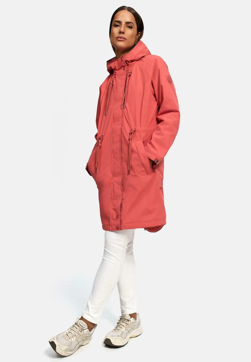 Long pink parka jacket with a hood, adjustable drawstrings, two front pockets, and a button closure. Worn over white leggings and sneakers.
