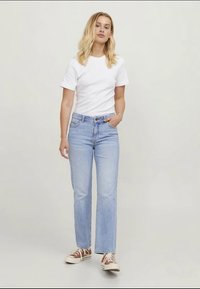 Svijetlosmeđe traperice ravnog kroja, uparene s bijelom pamučnom majicom i smeškim cipelama na vezanje. Jednostavan dizajn, bez uzoraka.