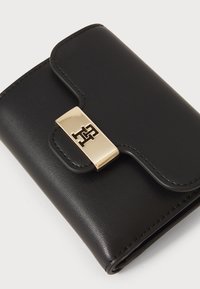 Zwarte leren portemonnee met afgeronde hoeken, een gouden sluiting met een logo en stiksels langs de randen, die een gladde textuur laat zien.