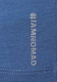 Blauwe katoenen stof met een gladde textuur, met de hashtag "#IAMNOMAD" in lichtgrijs gedrukt. Zichtbare gestikte randen.